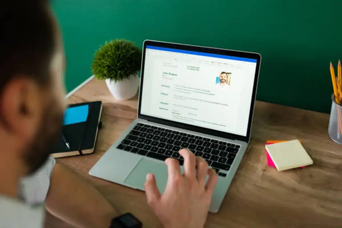 Homem digitando em laptop com currículo aberto na tela, simbolizando otimização de currículos para sistemas de recrutamento automatizados