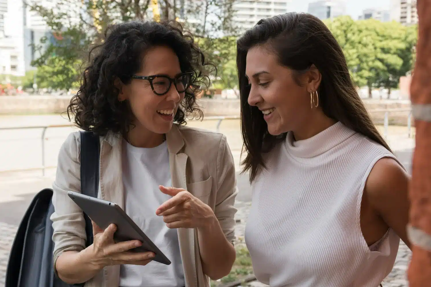 Duas mulheres sorrindo enquanto visualizam conteúdo em um tablet, refletindo a importância de hábitos para o sucesso profissional e financeiro.