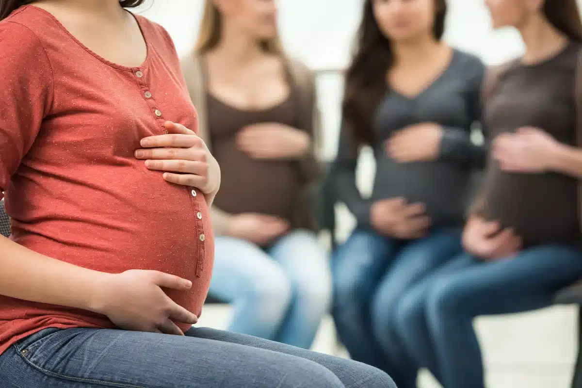Mulheres grávidas compartilhando experiências em grupo Grupo de mulheres grávidas sentadas, com as mãos na barriga, em um ambiente tranquilo.
