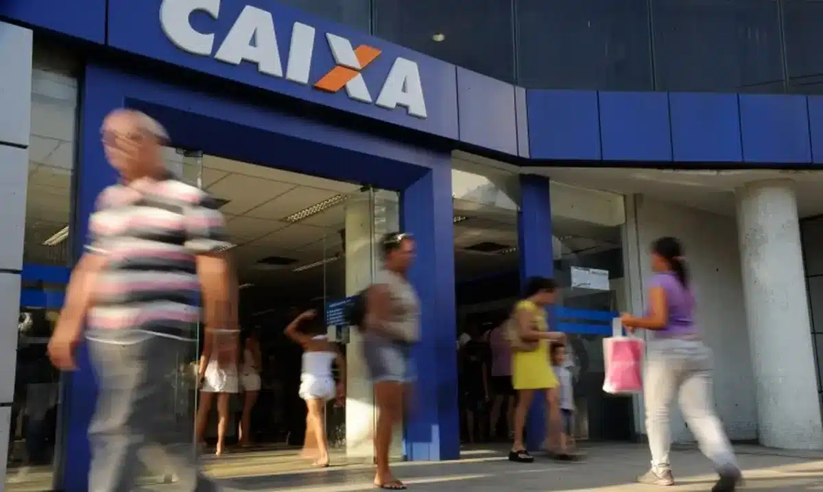Processo seletivo da Caixa Pessoas caminhando na entrada de uma agência da Caixa Econômica Federal.