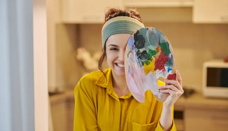 A psicologia das cores e a expressão criativa através da pintura Mulher sorrindo enquanto segura uma paleta de pintura cheia de cores vibrantes, refletindo a psicologia das cores
