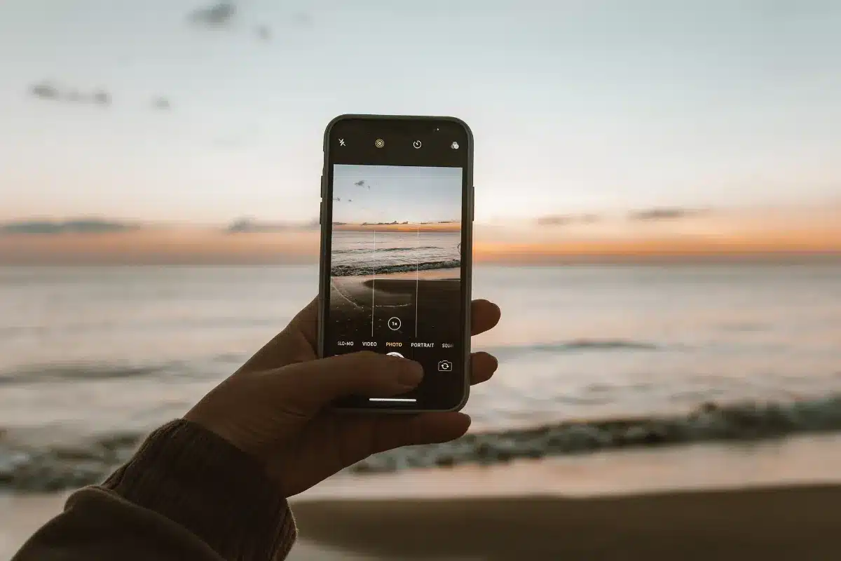 Capturando o pôr do sol perfeito à beira-mar Pessoa registra o pôr do sol na praia usando o celular.