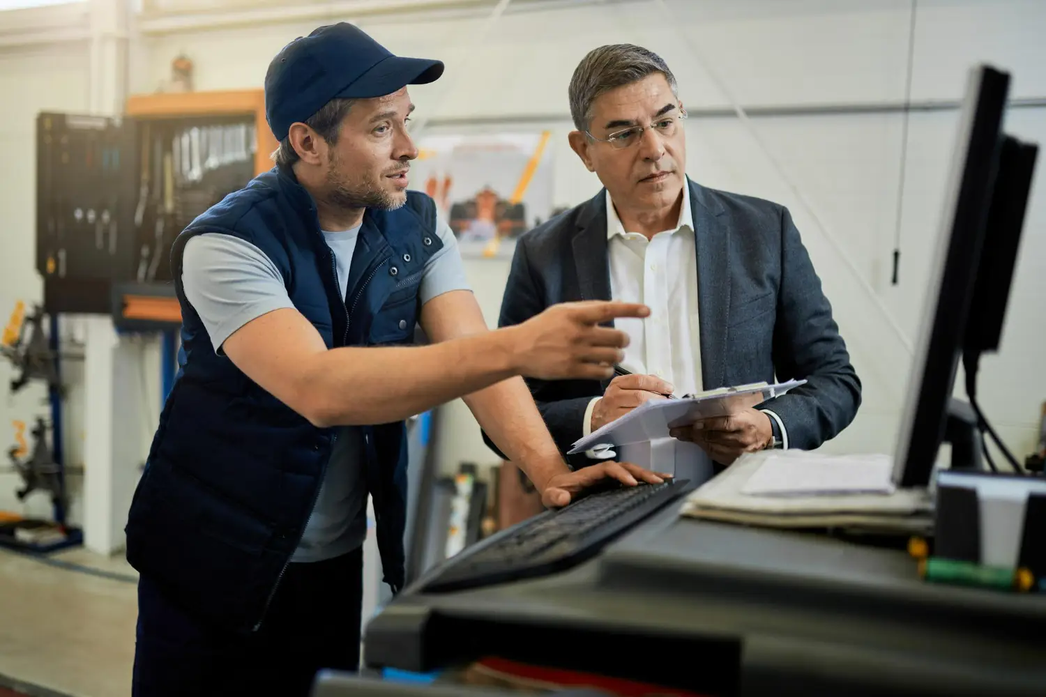 Dois profissionais conversando em um ambiente industrial, com um operador explicando algo para o supervisor em frente a um computador.