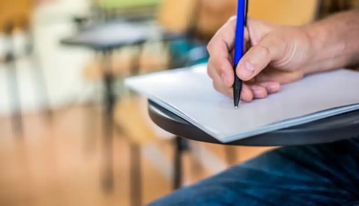 Mão segurando uma caneta e escrevendo em uma folha de papel, simbolizando o aprendizado sobre a forma correta de escrever "sutis". Escrita e reflexão: entendendo o plural de "sutil".