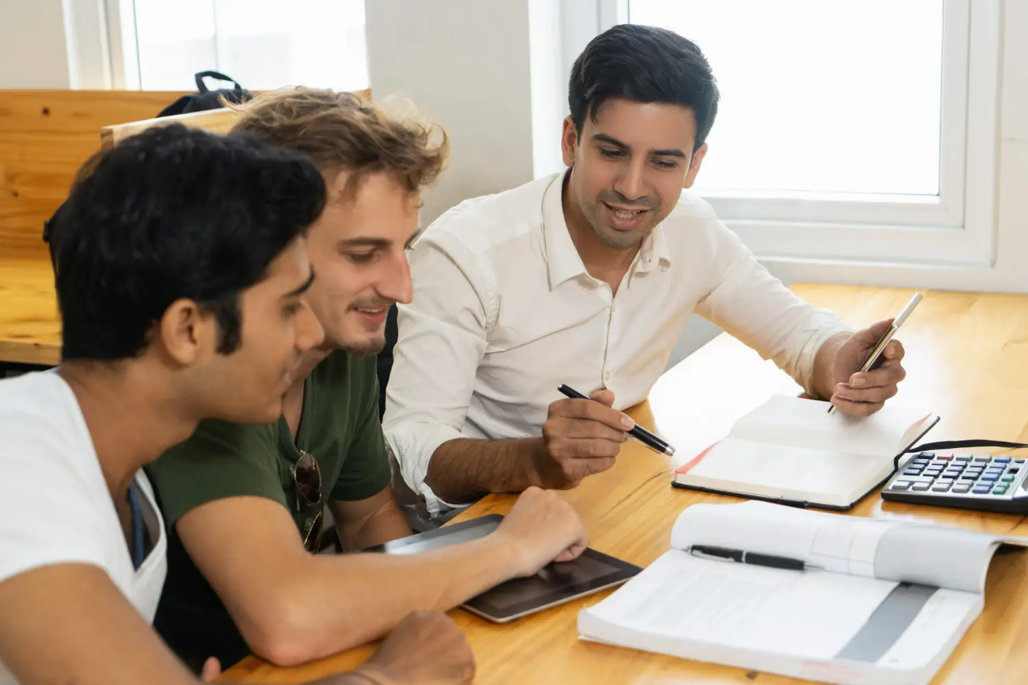 Três estudantes conversando e estudando juntos, com livros e materiais de estudo sobre a mesa, representando a oportunidade de aprendizado oferecida pelos cursos técnicos e superiores do IFMG.