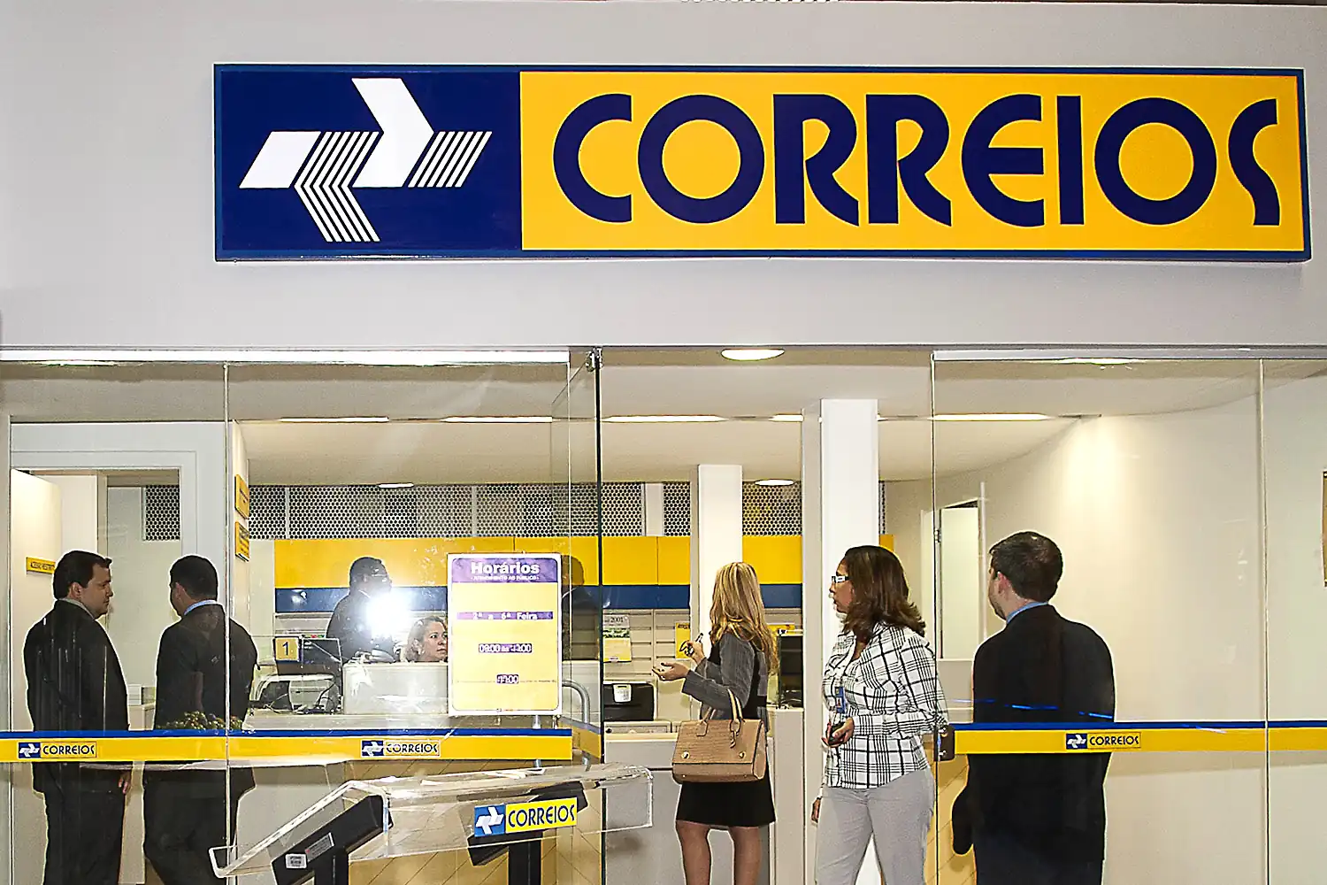 Atendimento nos Correios durante o feriado. Clientes em fila aguardam atendimento em agência dos Correios.