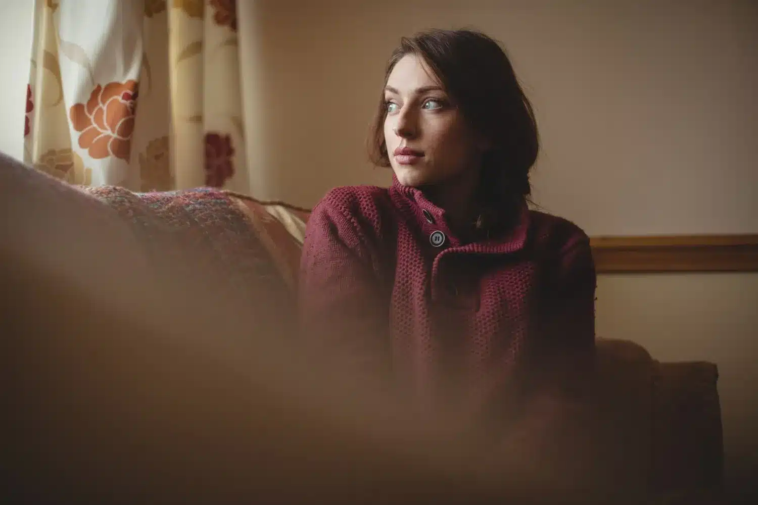 A Psicologia do Autodiálogo: Reflexões e Autoconhecimento Mulher pensativa sentada em um sofá, refletindo sobre seus pensamentos, simbolizando a prática do autodiálogo.