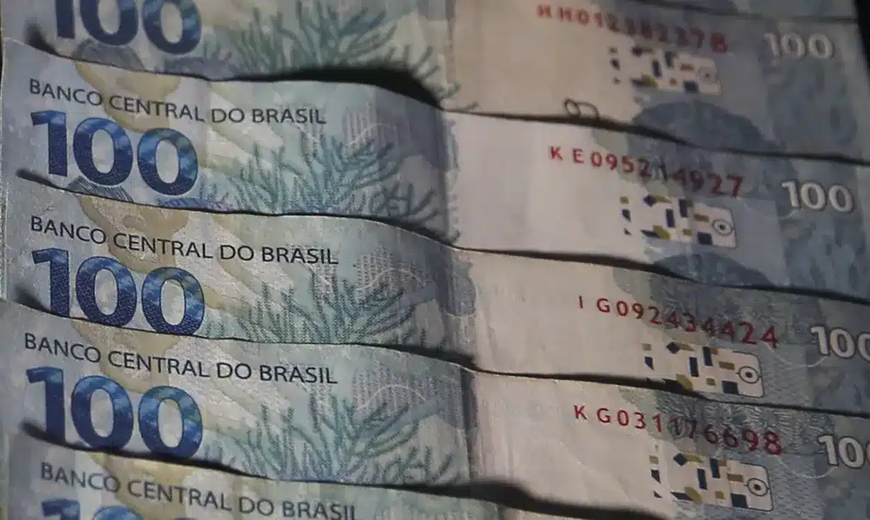 Notas de 100 reais empilhadas representando liberação de saques pela Caixa.