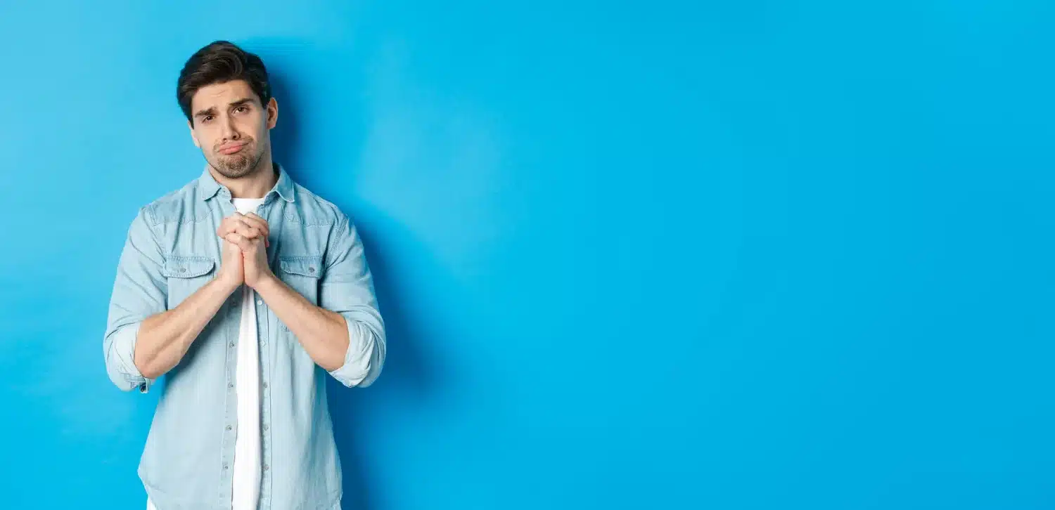 Homem com expressão de dúvida, segurando as mãos juntas em frente a um fundo azul claro. A imagem ilustra uma reflexão sobre o plural de palavras em português.