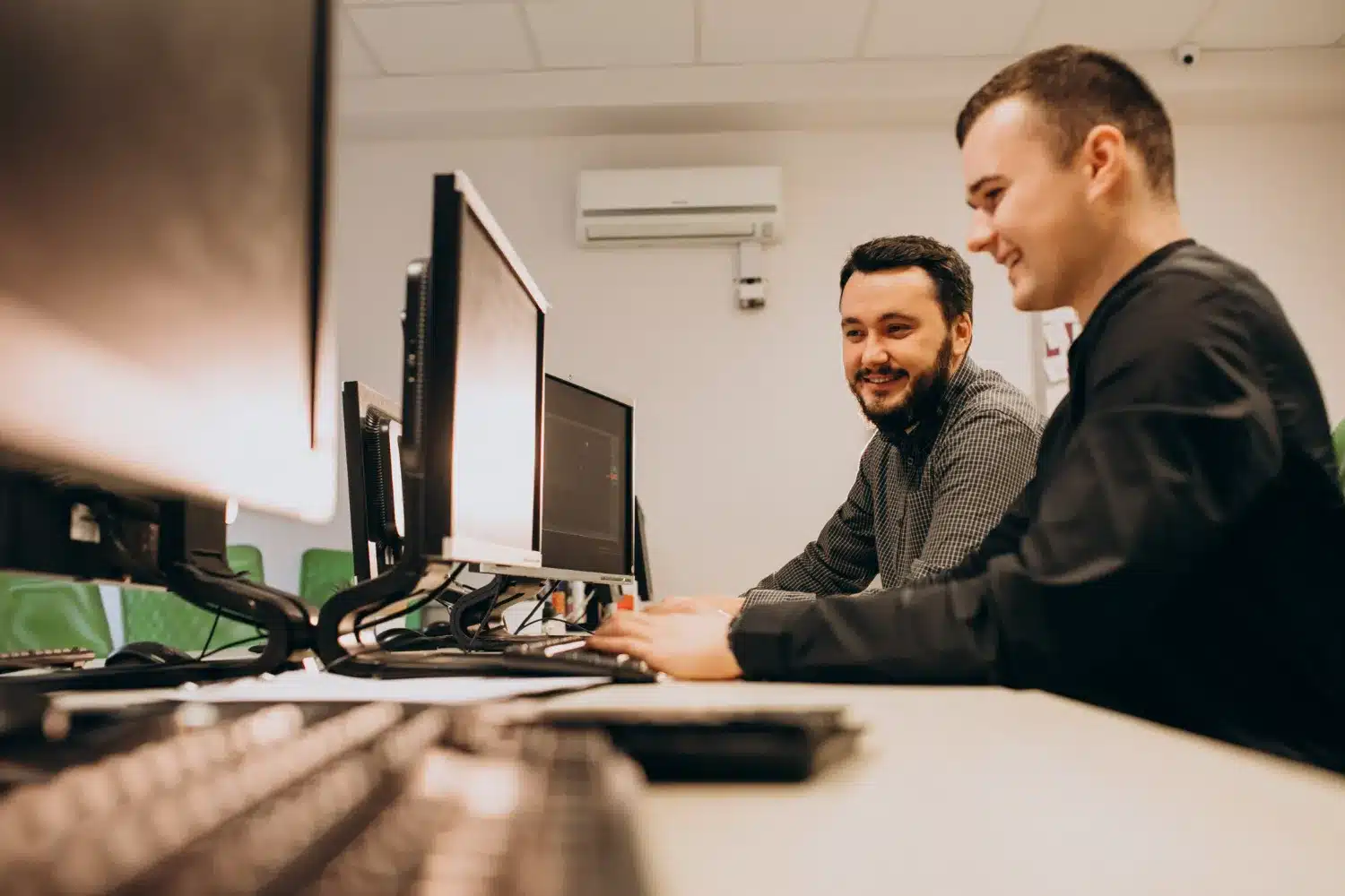 Dois jovens profissionais trabalhando juntos em computadores em um ambiente de escritório.