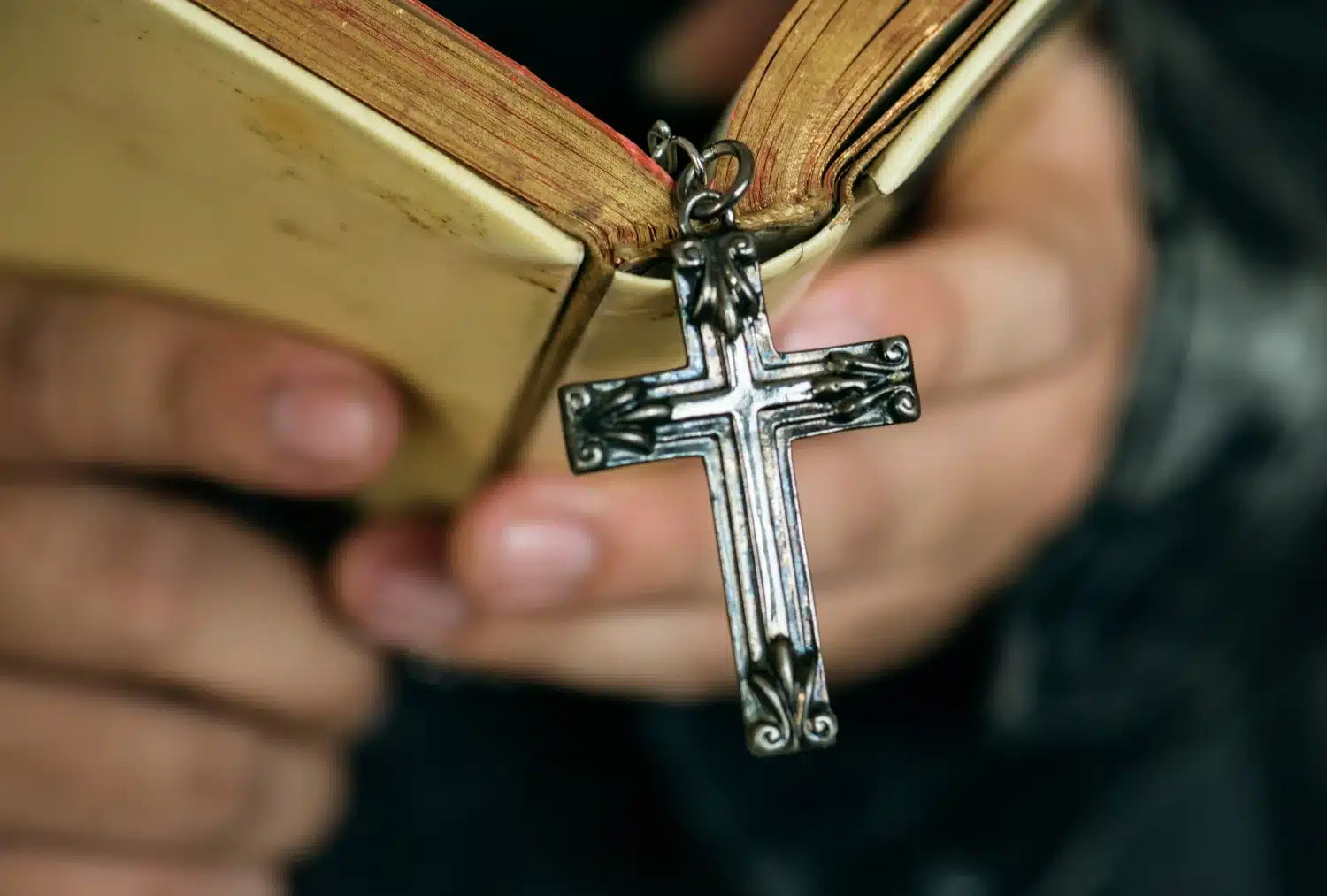 Cruz metálica em Bíblia representando a origem da palavra 'cristão'. Detalhe de uma cruz metálica pendurada em uma Bíblia, simbolizando a origem cristã da palavra 'cristão'.