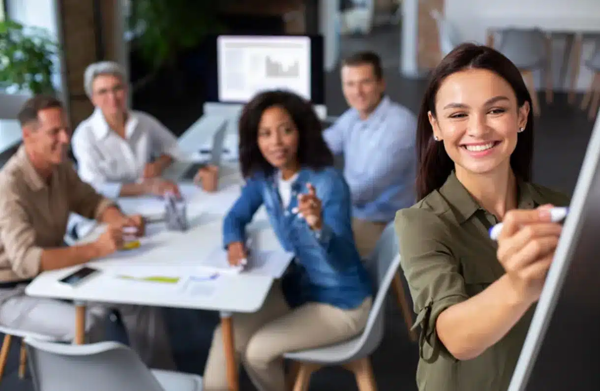 Reunião de equipe com apresentação e comunicação eficaz Profissionais colaborando em uma reunião, com uma mulher apresentando uma ideia na lousa, simbolizando habilidades de comunicação em equipe.