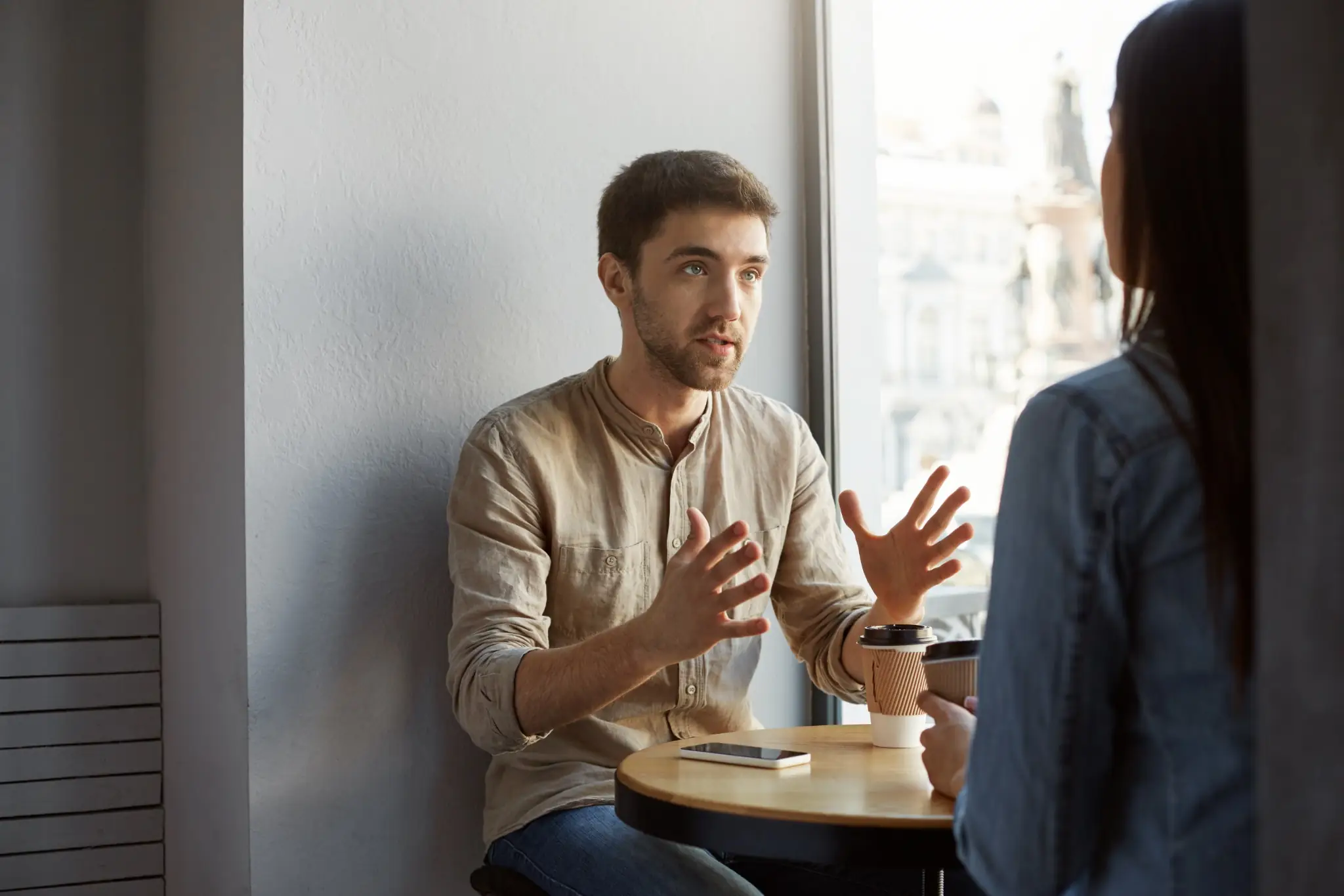 Diálogo com argumentos em um ambiente informal Homem explicando algo com gestos durante conversa em cafeteria.