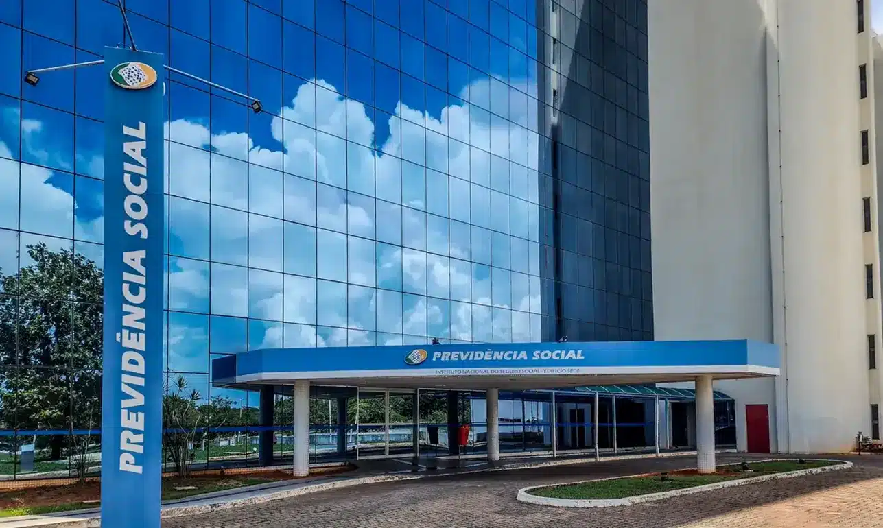 Fachada moderna do prédio da Previdência Social refletindo céu azul com nuvens.