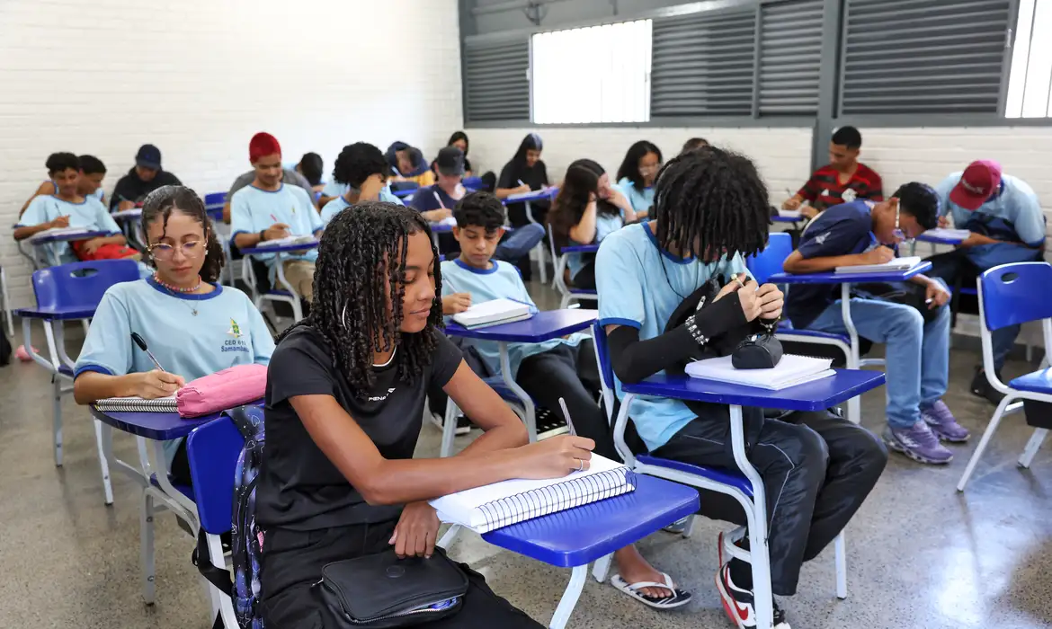 Estudantes ensino médio Estudantes uniformizados participando de uma atividade escolar em sala de aula.