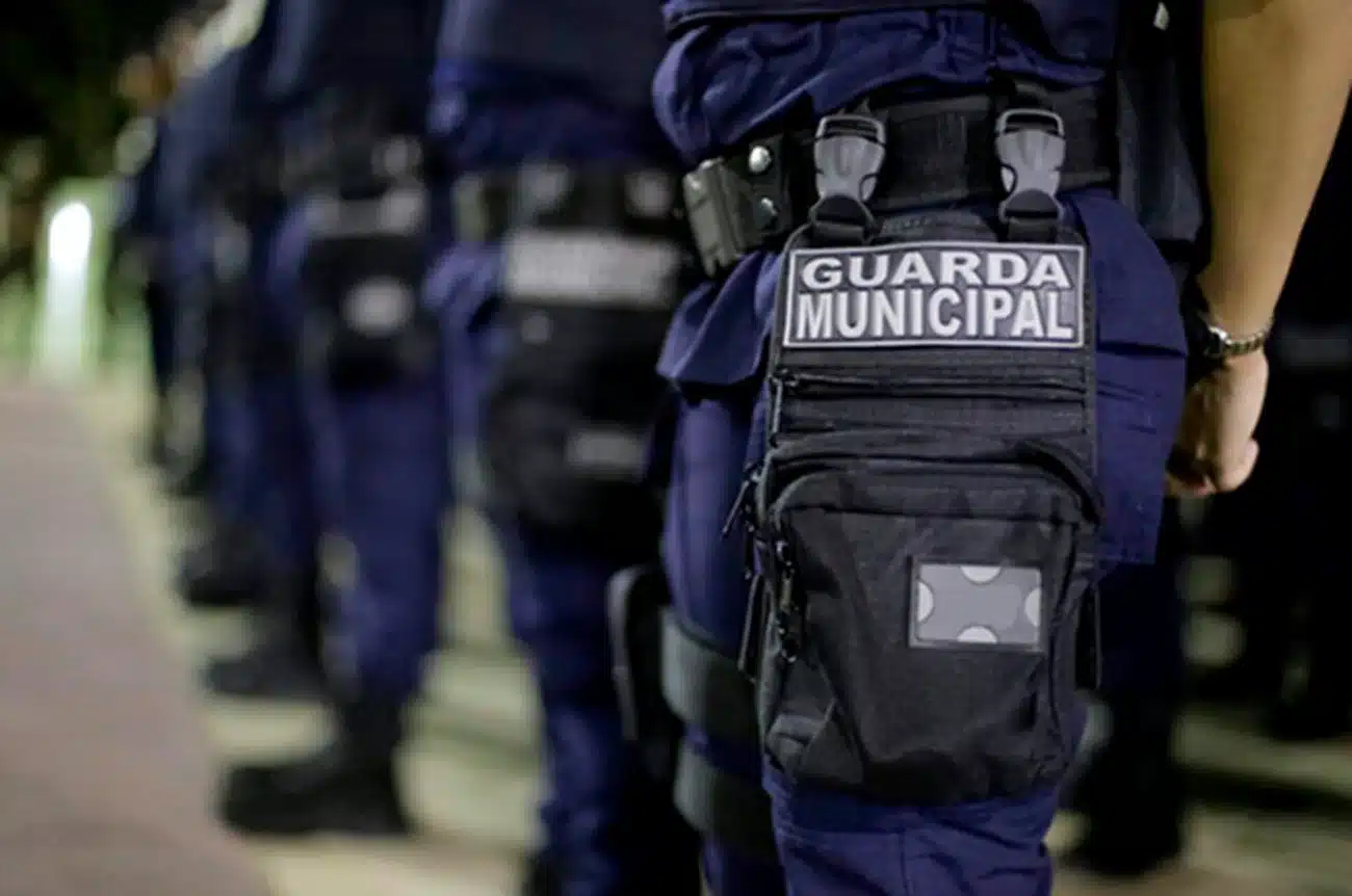 Foto de um guarda municipal em ação, com uniforme e bolso destacado com o emblema 'GUARDA MUNICIPAL'.