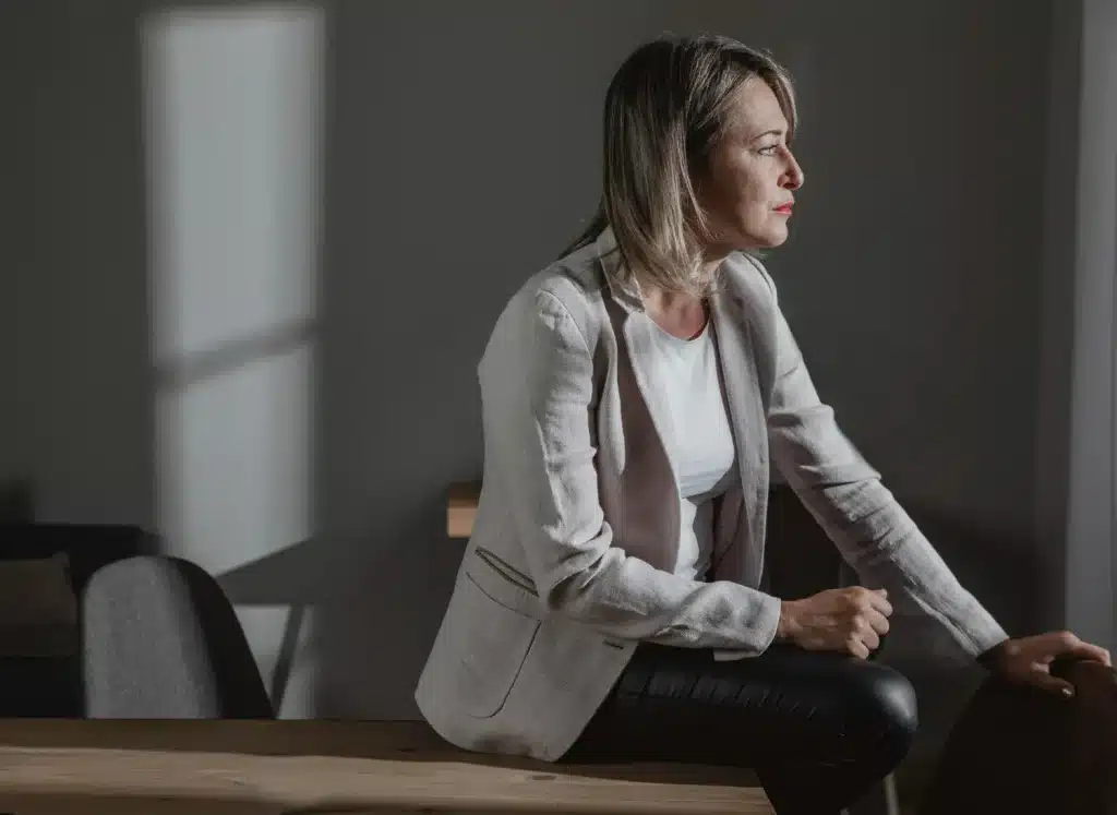 Reflexão silenciosa sobre a solidão na maturidade. Mulher de meia-idade sentada pensativa em ambiente escuro, representando os efeitos emocionais da solidão.