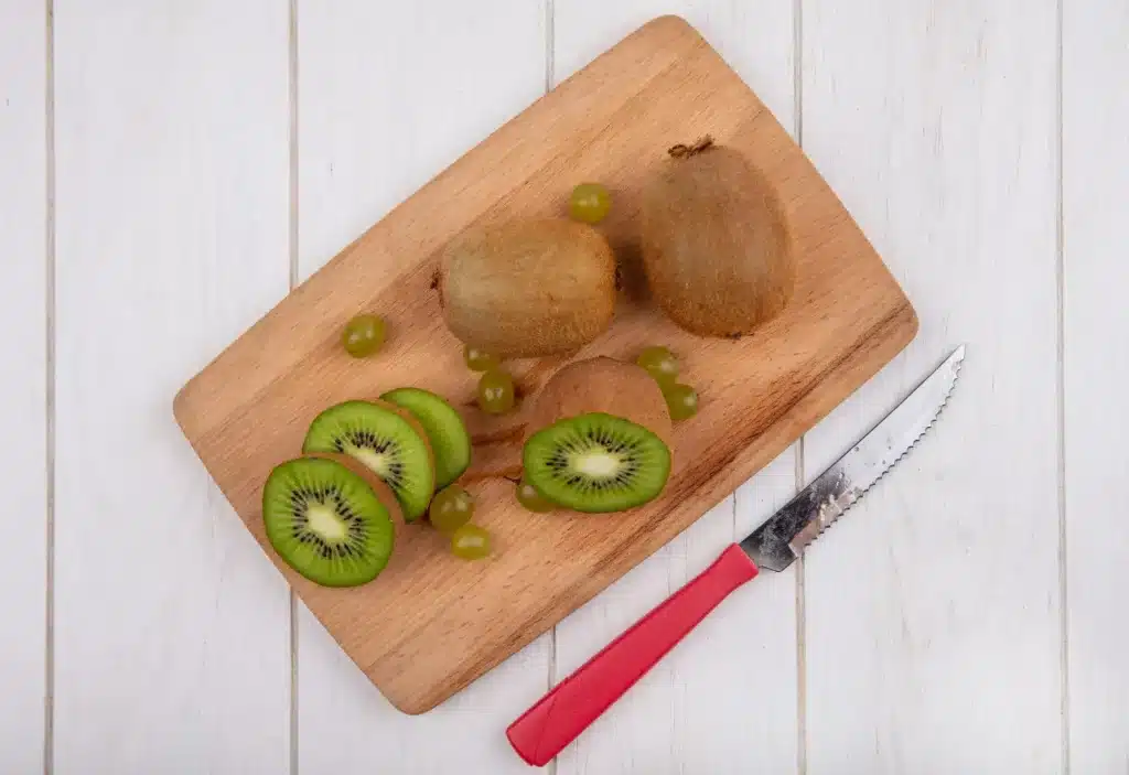 Fatiando kiwi: dúvidas sobre a grafia correta Kiwi fatiado em uma tábua de corte com uvas e uma faca ao lado.