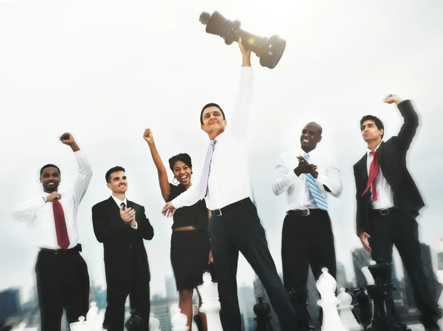 Usando 'Nós' para Vencer Juntos como Equipe Equipe celebrando uma conquista juntos, com o líder segurando um grande peão de xadrez, simbolizando o trabalho em equipe e a colaboração.
