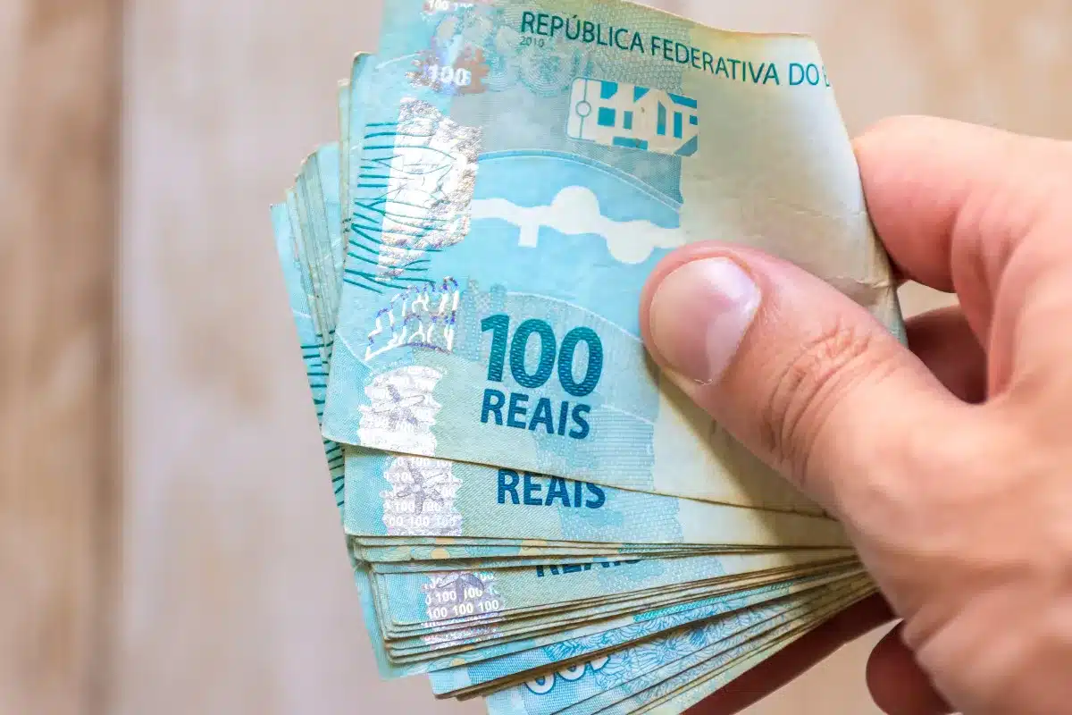 Mão segurando várias notas de 100 reais.