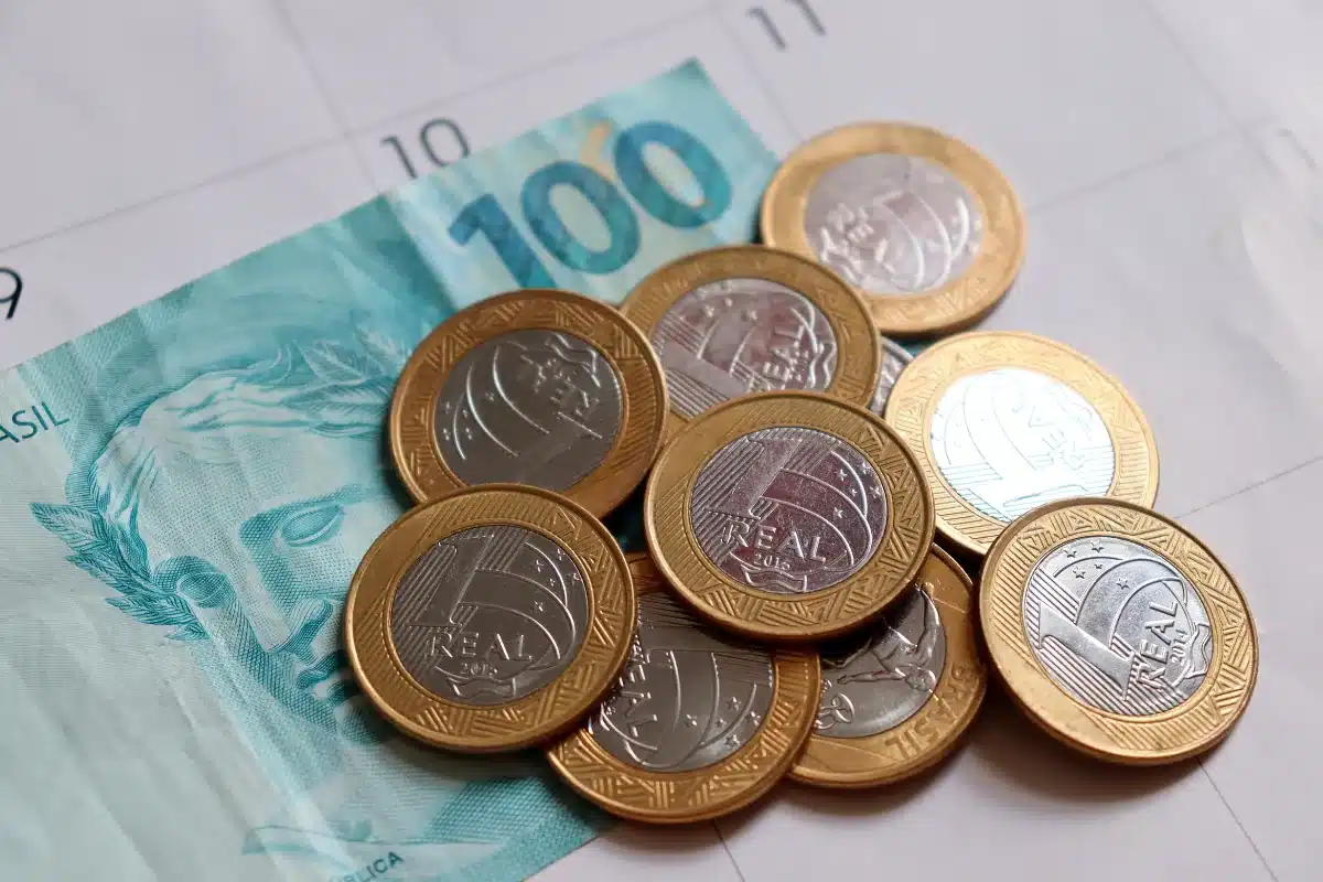 Calendário de pagamentos Moedas de 1 real e nota de 100 reais sobre calendário