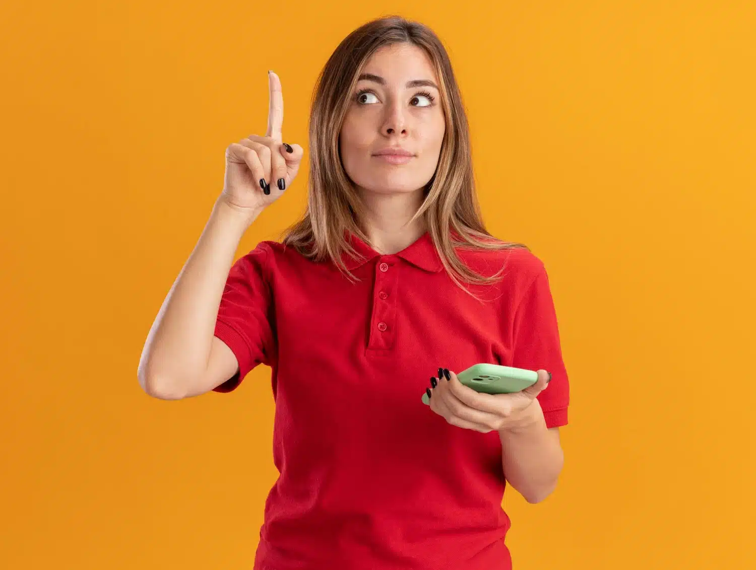 Mulher jovem com camisa vermelha segurando celular e apontando o dedo indicador para cima, simbolizando uma ideia ou atenção.