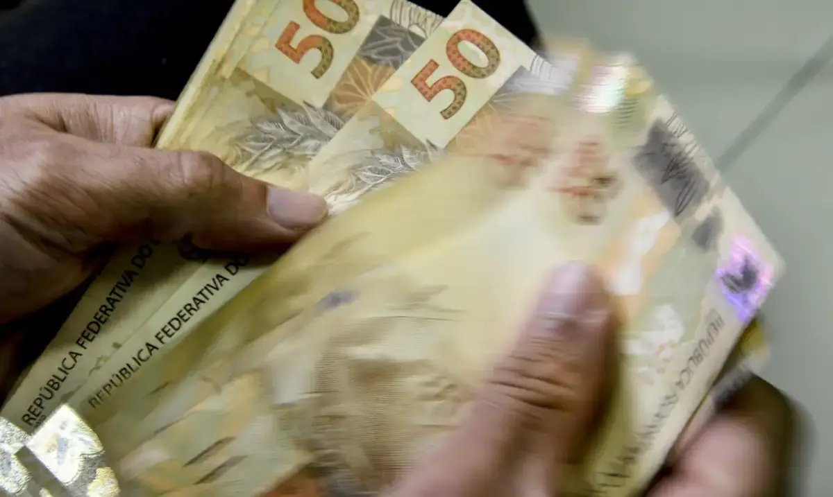 Pessoa manuseando notas de 50 reais em dinheiro físico.