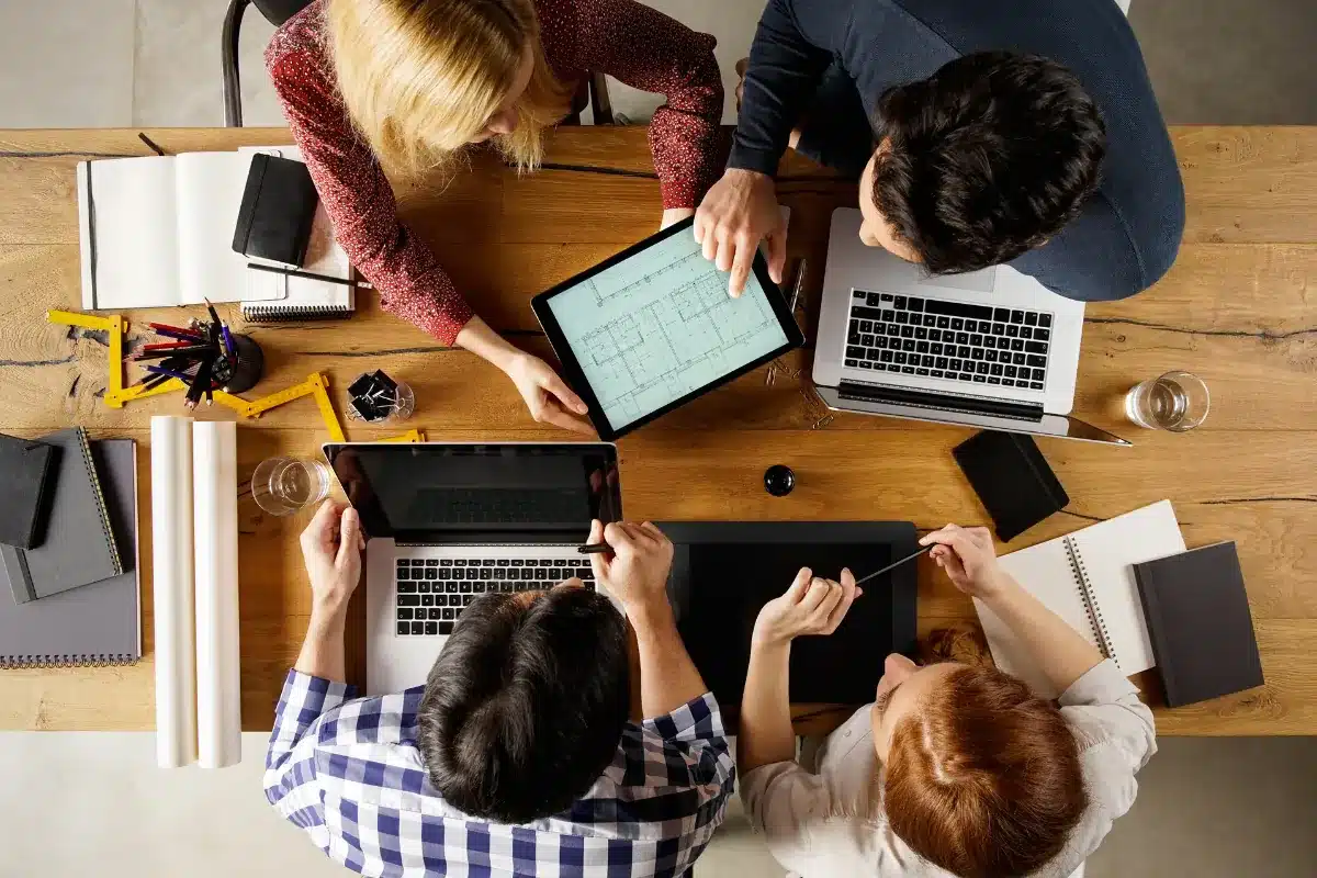 Técnico em Design de interiores Equipe reunida em mesa de trabalho analisando projetos digitais.