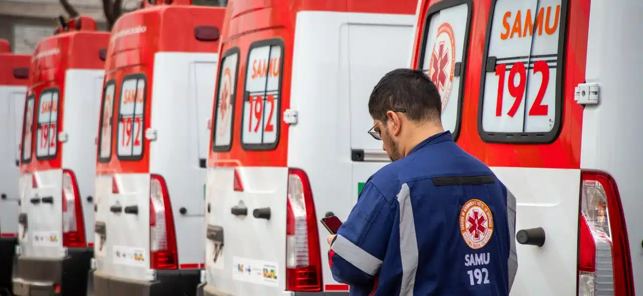 Ambulância do SAMU com profissional de saúde em primeiro plano, trabalhando em uma missão de emergência.