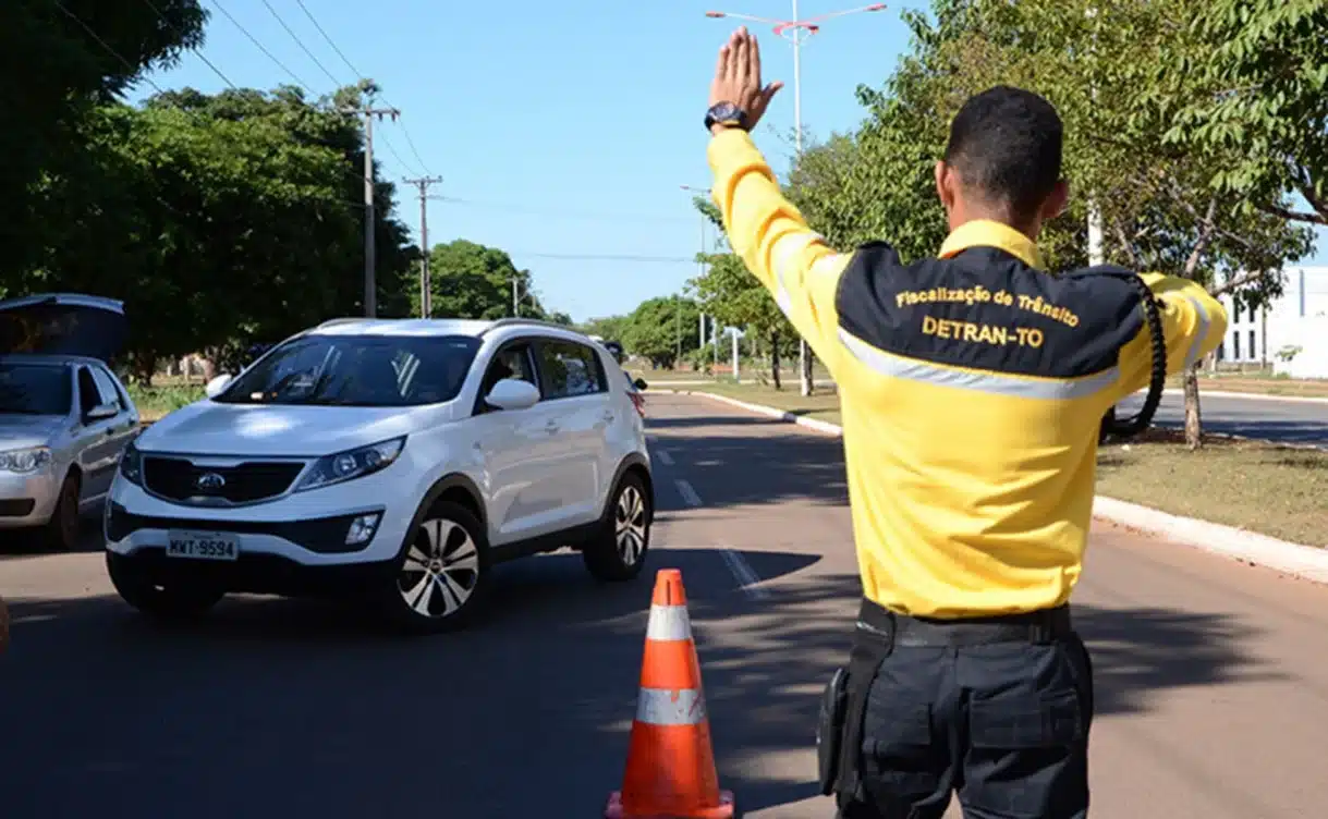 Agente de trânsito orientando o tráfego com cone, representando fiscalização do DETRAN-TO.