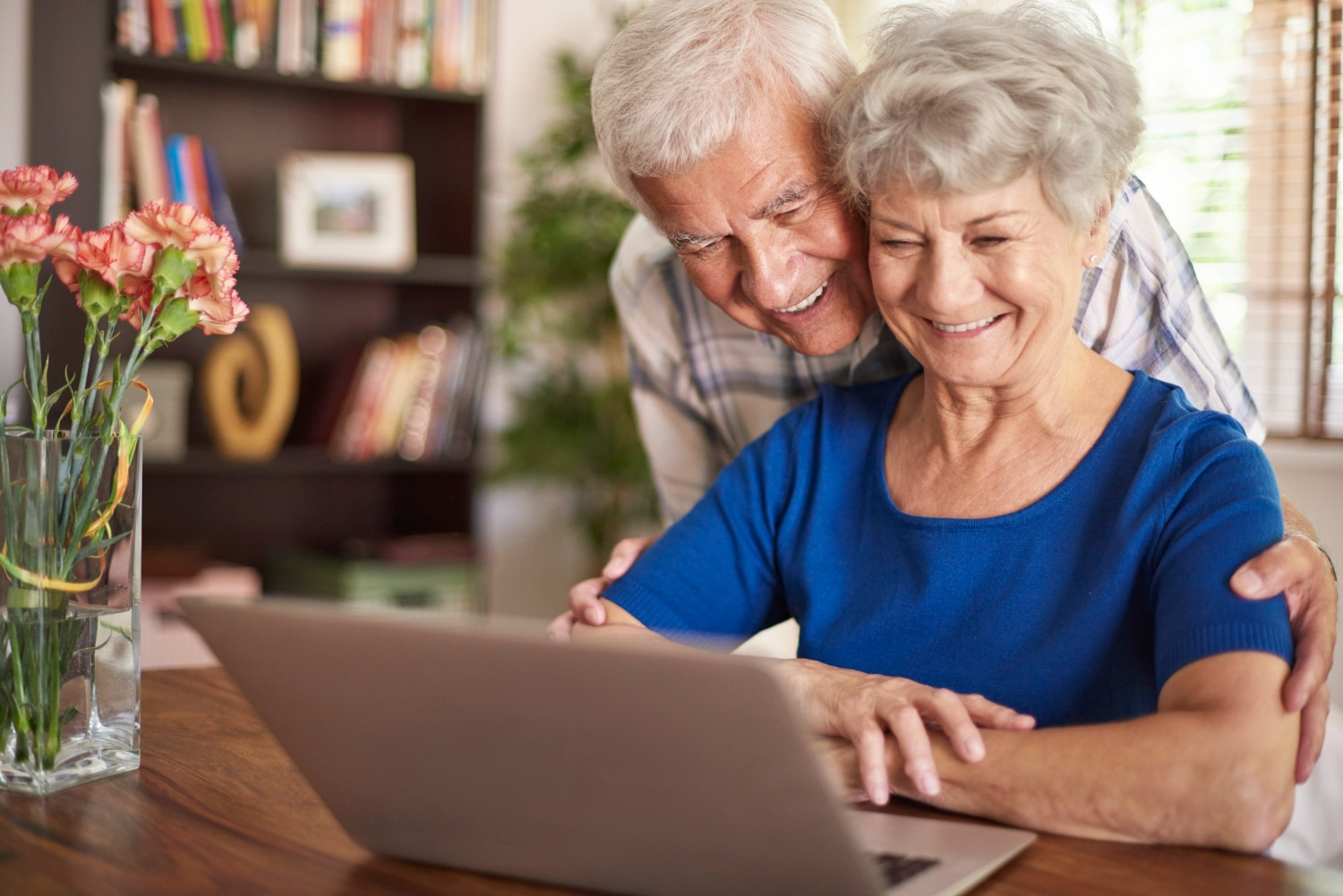 Casal de idosos sorridente utilizando notebook em casa.