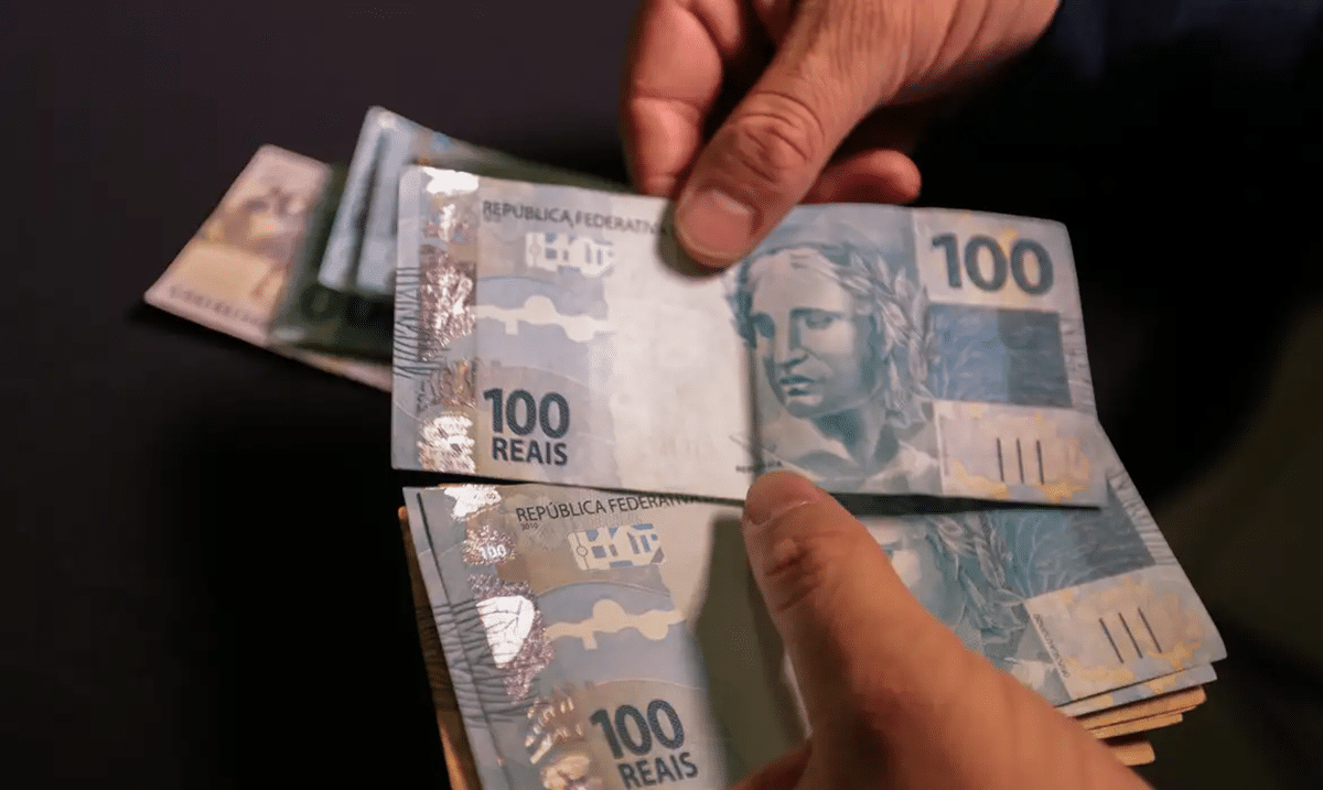 Pessoa retirando cédulas de R$100 de uma carteira, simbolizando a comparação entre diferentes faixas de renda.
