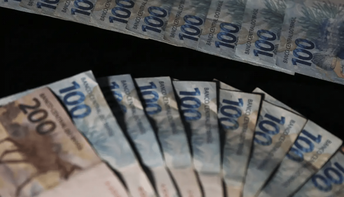 Notas de real em foco, incluindo cédulas de R$ 100 e R$ 200, ilustrando benefícios financeiros para milhões de brasileiros.