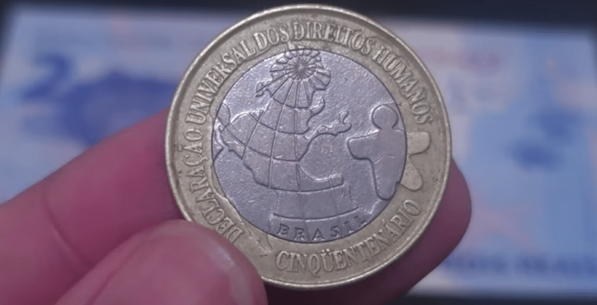 Moeda de 1 real comemorativa dos Direitos Humanos e cédula rara de 2 reais CJ ao fundo