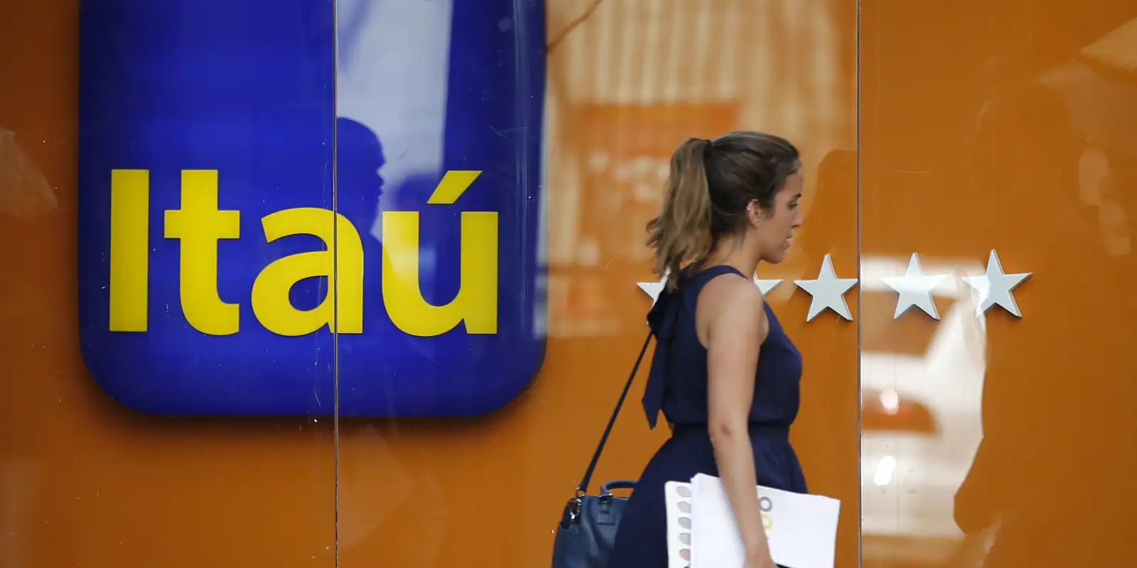 Mulher passa em frente à fachada com logo do banco Itaú e estrelas de avaliação.