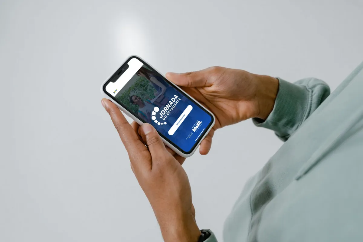 Aplicativo Jornada do Estudante no celular Pessoa segurando celular com o aplicativo Jornada do Estudante aberto na tela.