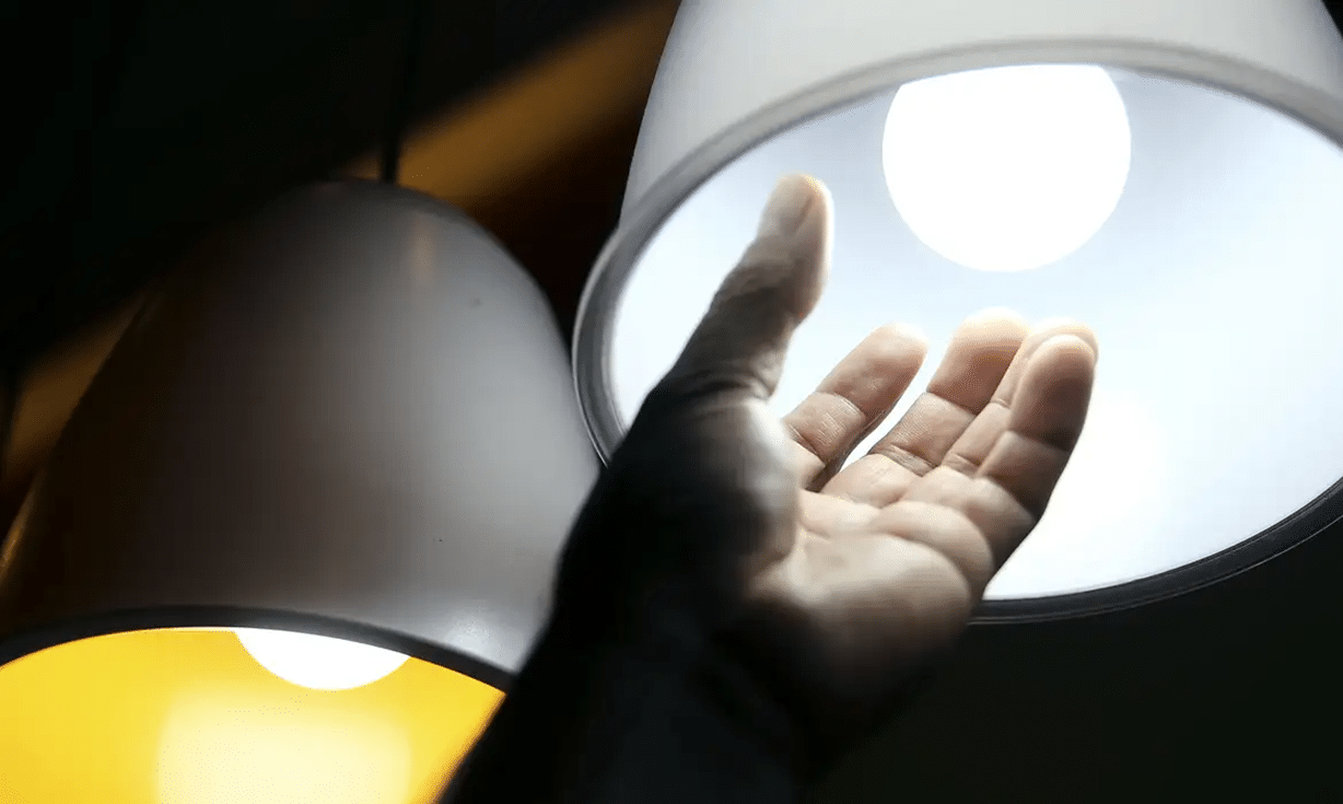 Mão próxima de lâmpada acesa, mostrando o brilho do LED branco.