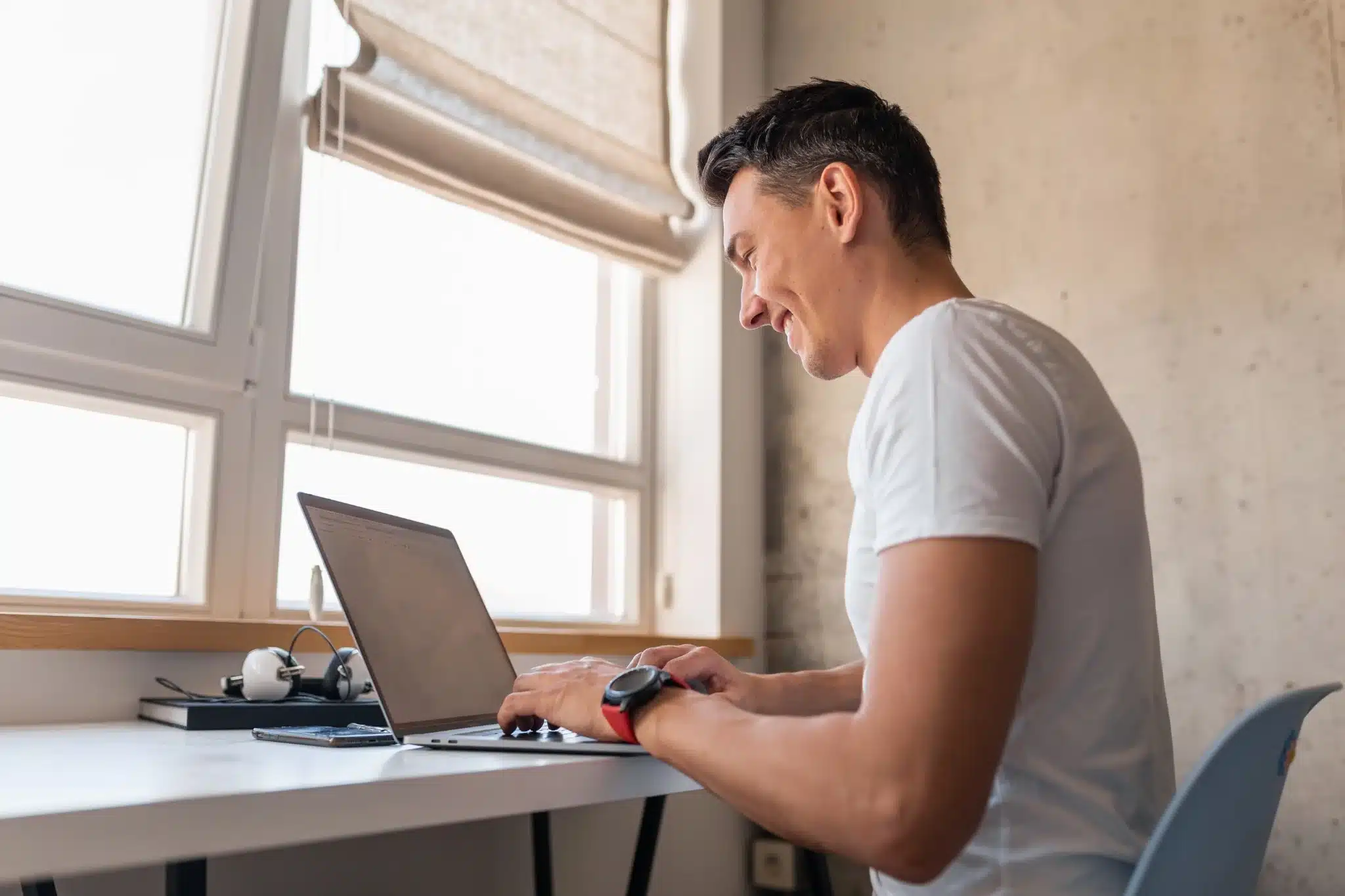 Concurso Guarda Municipal Homem sorrindo enquanto trabalha em um laptop, simbolizando a organização e preparação para o concurso.