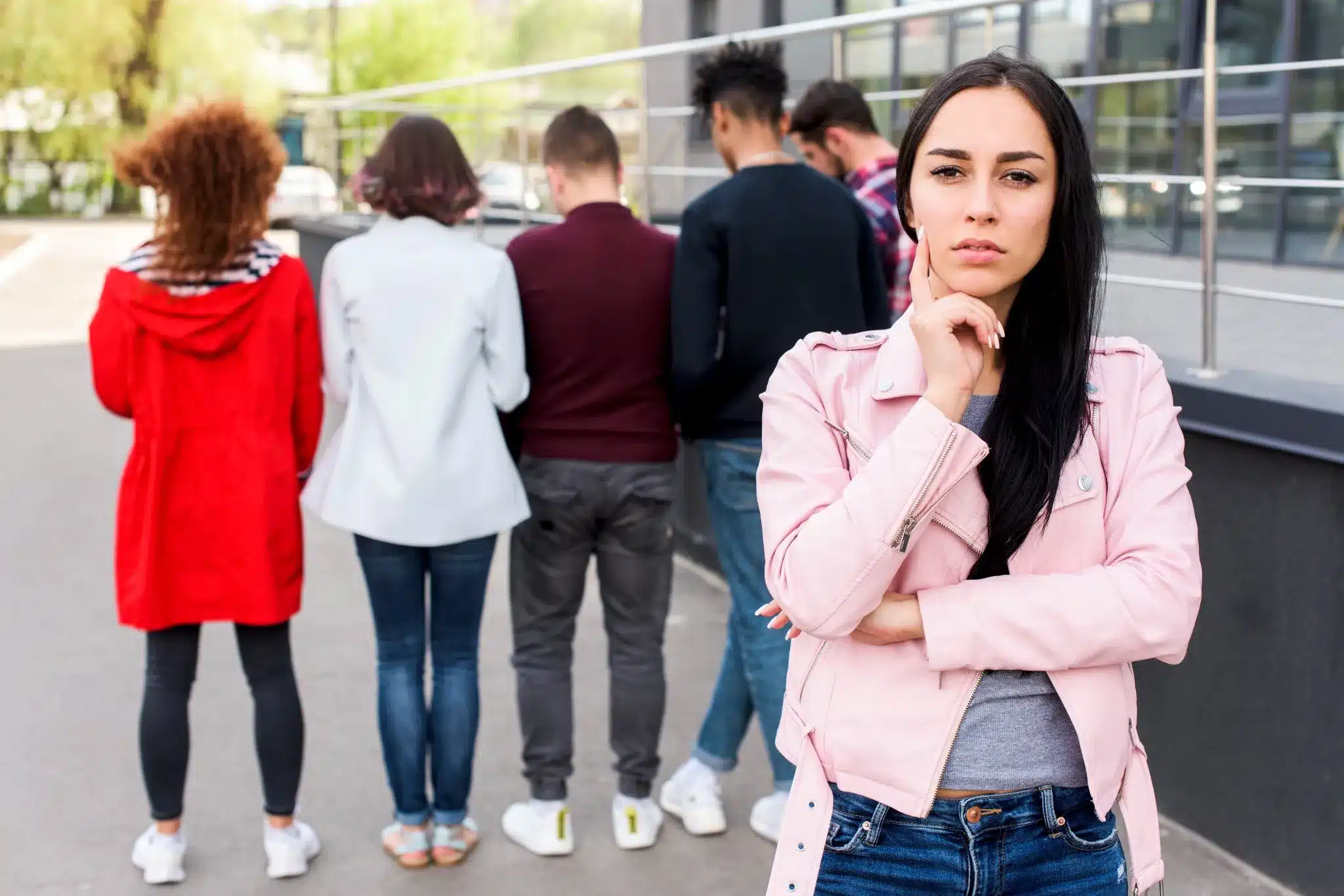 Proteger-se de interesseiros: Como lidar com relações baseadas em interesse. Mulher pensativa, refletindo sobre relações, enquanto observa um grupo de pessoas ao fundo. Ela está em um ambiente urbano, demonstrando cuidado ao estabelecer limites e evitar interesses.