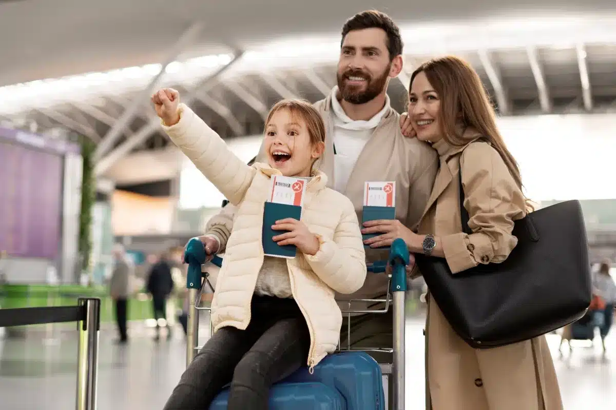 Família feliz em aeroporto com passagens e malas, pronta para viajar de forma econômica durante a queda do dólar.