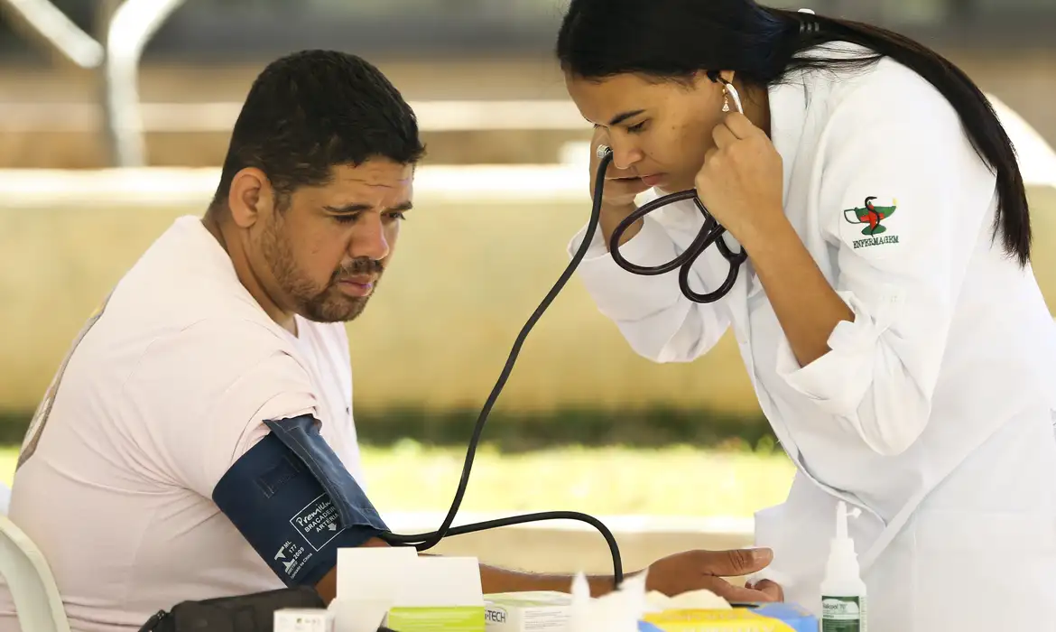 "Inspeção médica para concurso público Homem sendo examinado por uma profissional de saúde, medindo a pressão arterial, representando a inspeção médica oficial de concursos públicos.