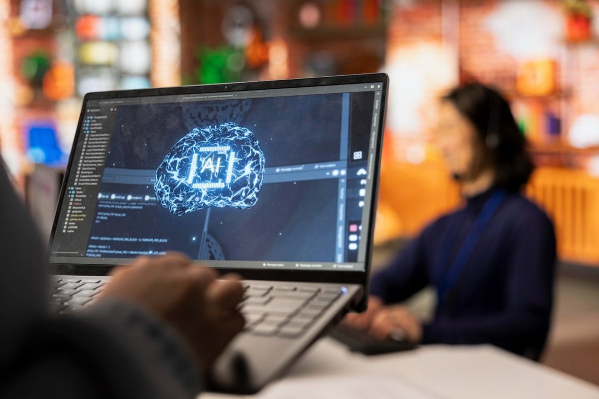 IA e automação definem futuro das profissões até 2030 Laptop exibindo interface de inteligência artificial com cérebro digital luminoso e código de programação em ambiente de trabalho