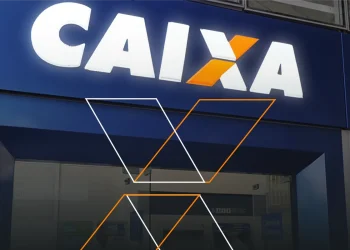 Fachada de agência da Caixa Econômica Federal com logo iluminado em azul e branco à noite.