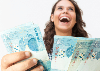 Mulher sorridente segurando várias notas de 100 reais olhando para cima com expressão de felicidade