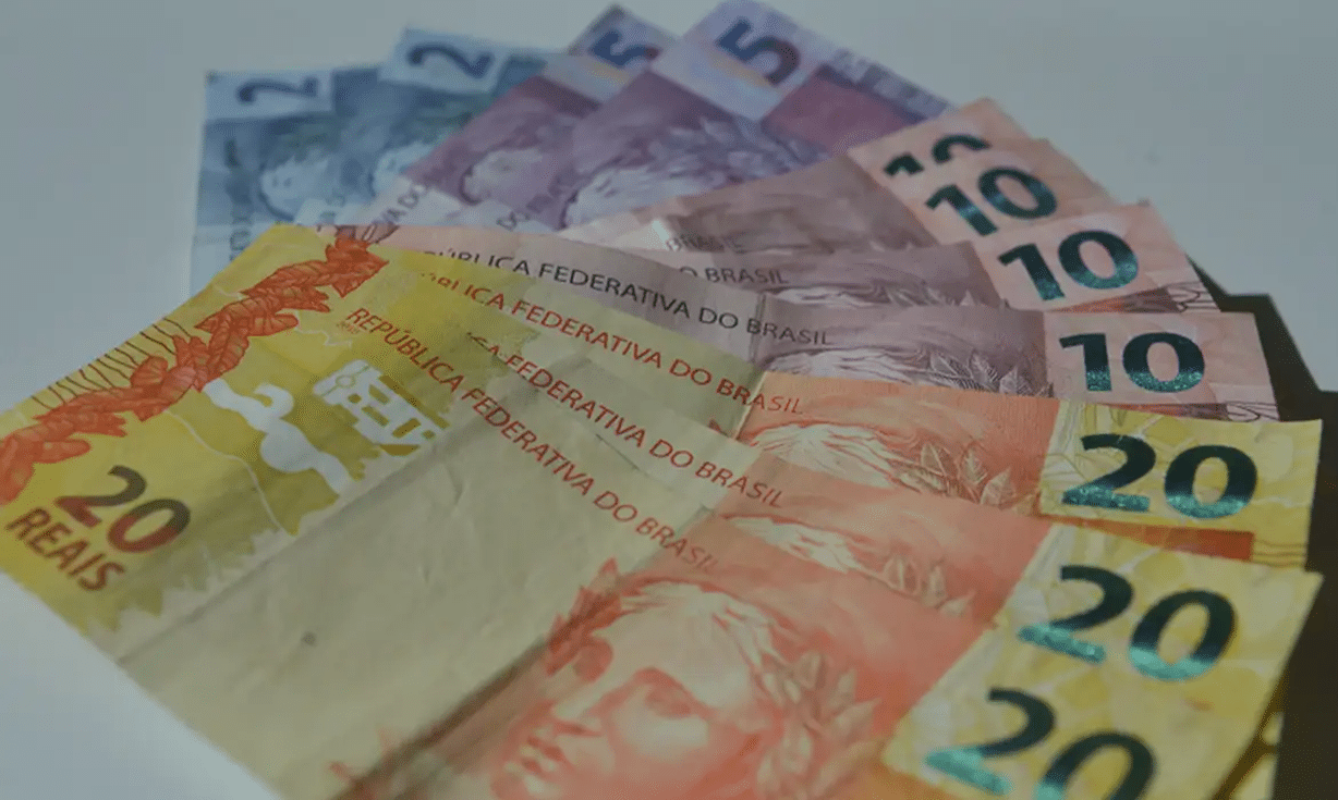 dinheiro agência brasil Notas de reais brasileiros em cédulas de 5, 10 e 20 espalhadas sobre superfície branca.