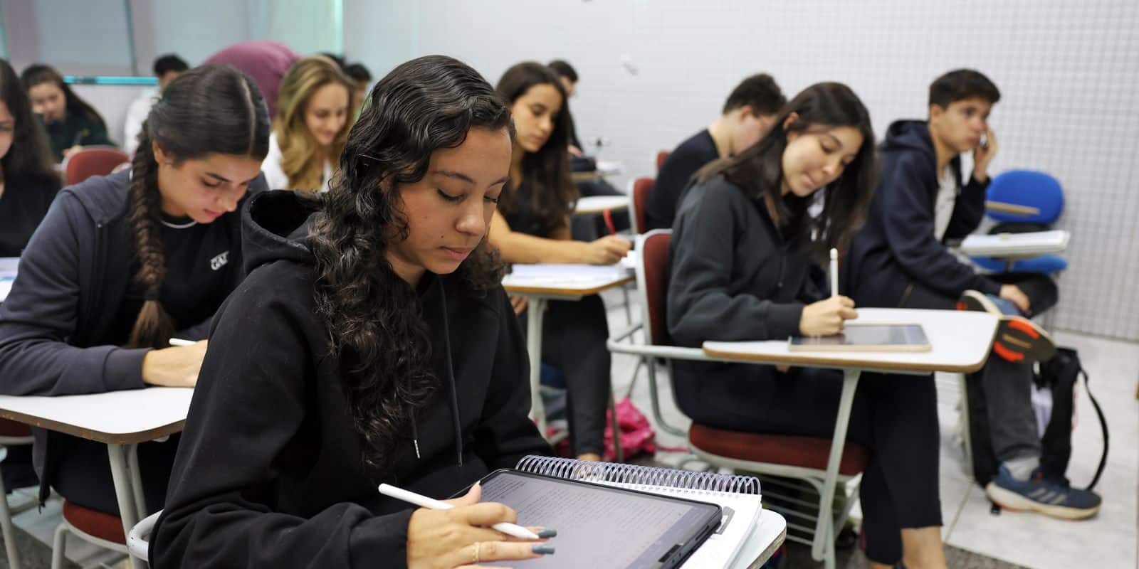 Alunos jovens focados escrevendo em tablets durante aula em sala de aula com cadeiras e carteiras organizadas
