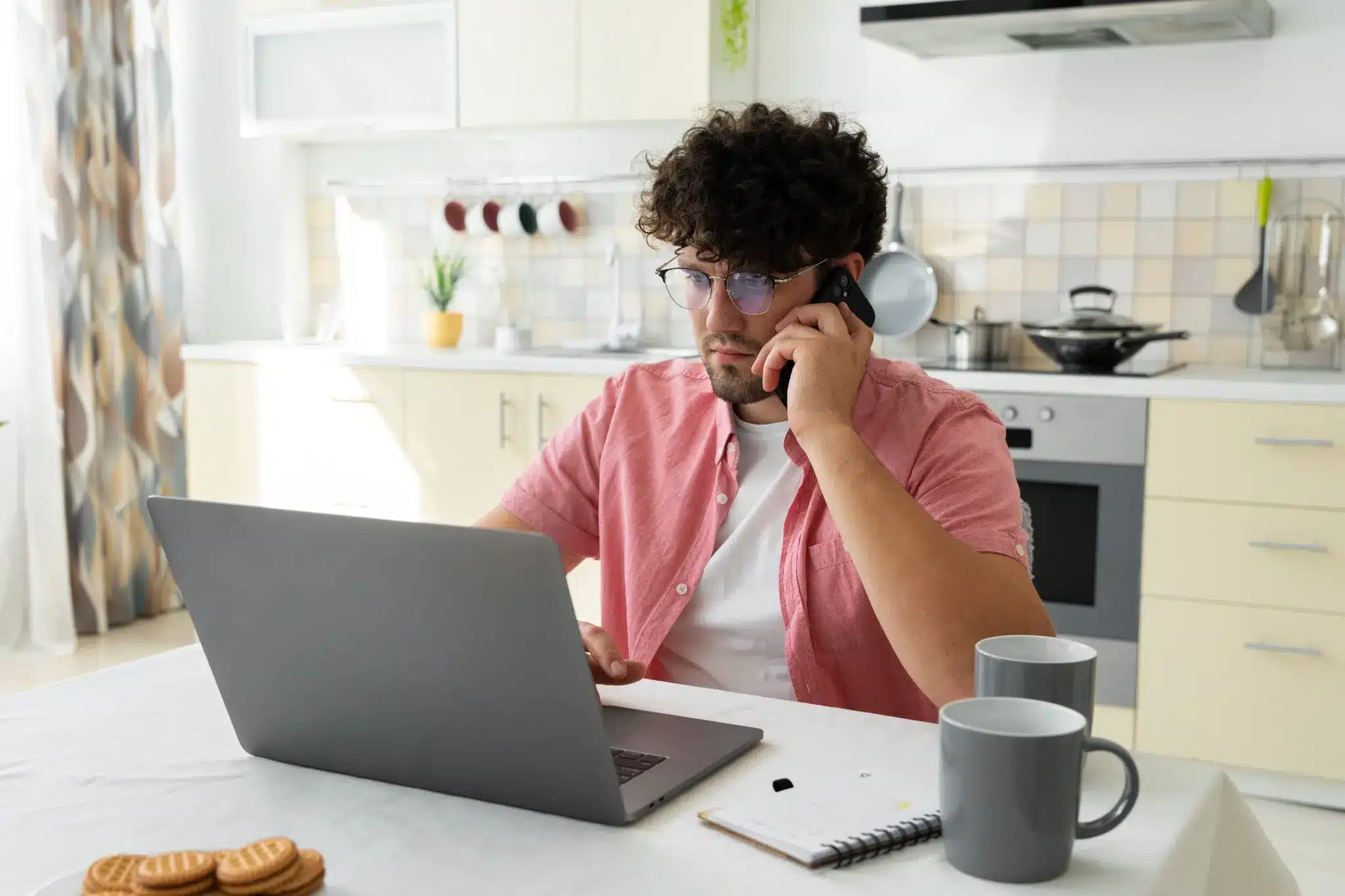 Home Office: Dicas para aprimorar habilidades e buscar oportunidades de trabalho remoto Homem trabalhando de home office, falando no telefone e utilizando um laptop, representando a busca por especializações online e plataformas de trabalho remoto.