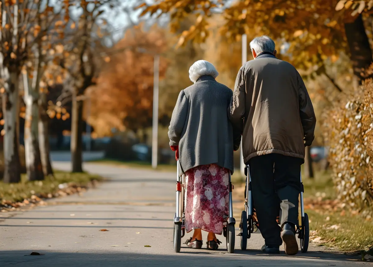 Casal de idosos caminhando com andadores em um parque arborizado durante o outono, simbolizando tranquilidade na aposentadoria.