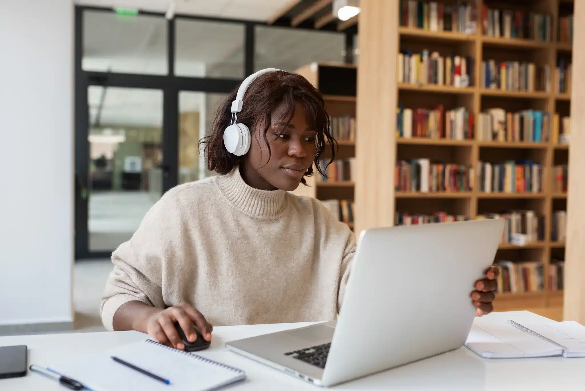 Aumento de Matrículas em Cursos EAD: A Transformação da Educação Superior no Brasil Jovem estudante utilizando computador portátil com fones de ouvido em ambiente de biblioteca, ilustrando a popularização dos cursos EAD no Brasil.
