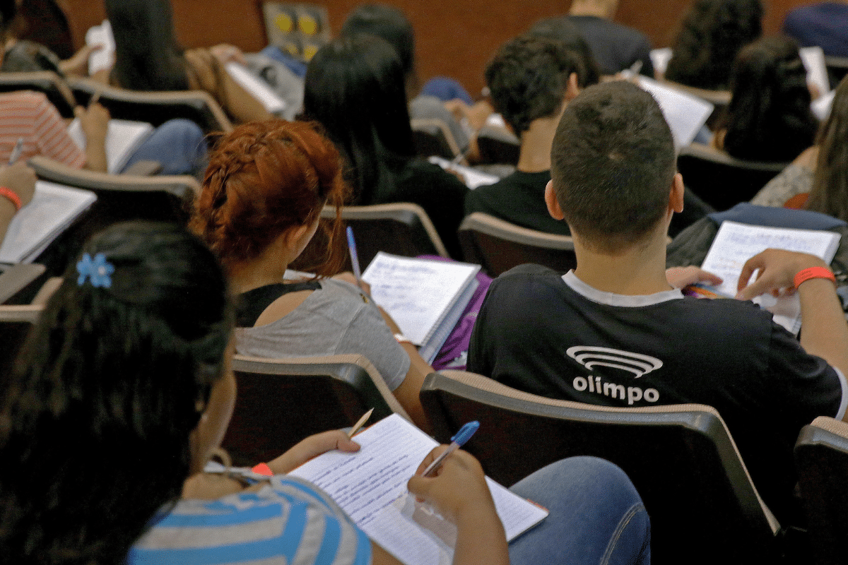 Curso de licenciatura Jovens em auditório acadêmico anotando em cadernos durante aula